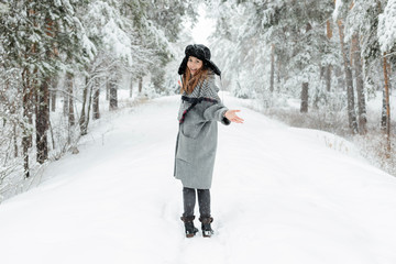 Beautiful young woman standing among snowy trees in winter forest and enjoying snow.