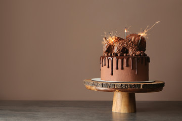 Sweet chocolate cake with sparklers on table against color background