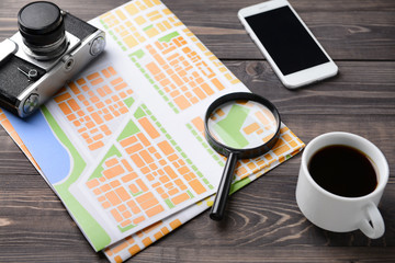 Composition with city map, photo camera, magnifier and mobile phone on wooden table. Travel concept