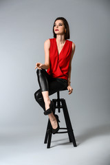 Fototapeta premium Fashionable young woman sitting on stool against grey background
