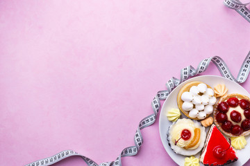 healthy lifestyle, diet, carbs reduce, sugar, sweets. pink background with delicious cakes and measure tape with copy space. fitness, nutritionist, dietitian blog design concept