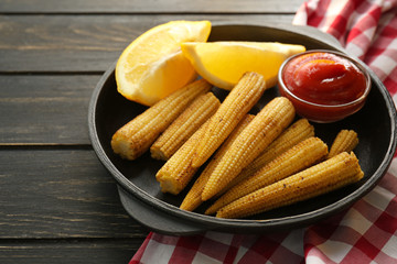 Frying pan with tasty corn cobs, lemon and sauce on wooden table
