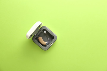 Box with hearing aid on color background