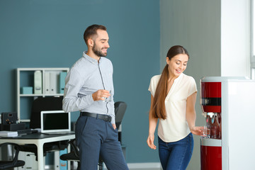 Colleagues drinking water from cooler in office
