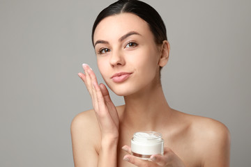 Portrait of beautiful woman with cream for healthy skin on grey background