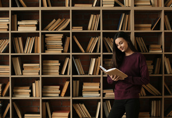 Portrait of beautiful young woman with book in library © Pixel-Shot