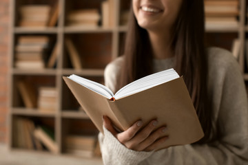Beautiful young woman reading book in library, closeup