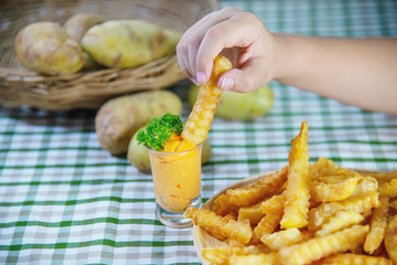 Hand holding delicious fried potato on wooden plate with dipped sauce - traditional fast food concept