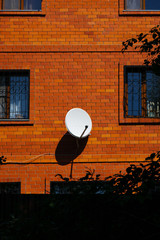 Vertical close up shot of red brick house with decorative window grates and white satellite dish