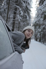 Beautiful girl looks out of the car on a winter road in the woods