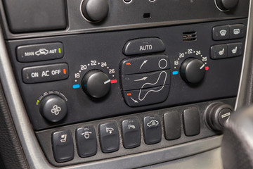 The central control console on the panel inside the car close-up with climate control and audio system and a hole for the CD and emergency button in gray and black.