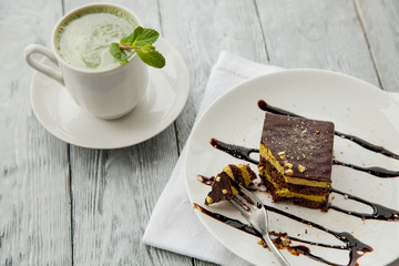 piece of Austrian three-layer cake and cup of matcha tea on a white plate in a cafe