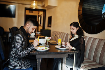 Lovely indian couple in love, wear at saree and elegant suit, sitting on restaurant and eating desserts together.