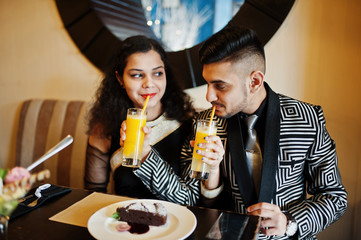 Lovely indian couple in love, wear at saree and elegant suit, sitting on restaurant and  drinks orange fresh juice from the tubule.