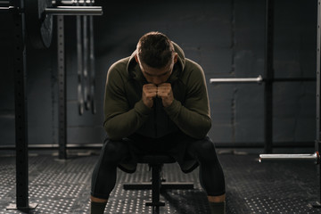Strong sporty man sitting on gym bench suffering breakdown to overcome.