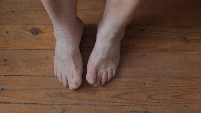 Old female legs stand on a wooden floor. View from above