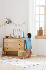 Little girl wearing light blue dress playing in children room scandinavian style. © laniko