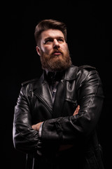 Obraz premium Portrait of Handsome bearded man wearing a leather jacket with serious expresion over black background