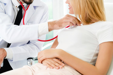 Male doctor is talking and examining female patient in hospital office. Healthcare and medical...