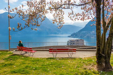 Girl enjoying city view from a bench under the Magnolia tree at the hill in Lugano, view at the Lake Lugano and Alps mountains in Ticino canton of Switzerland