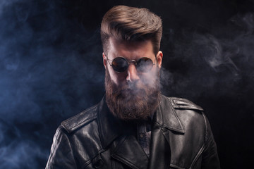 Rich handsome bearded man with sunglasses and leather jacket over black background