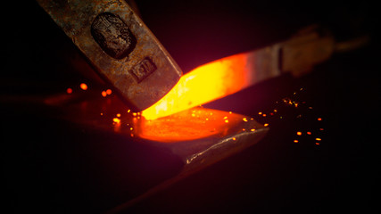 MACRO: Small black particles flying away from hot red blade while getting forged