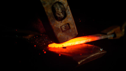 MACRO, DOF: Metalworker forging a glowing hot piece of metal into a knife blade.