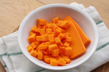 Fresh Butternut squash cut in pieces in a bowl on wooden table