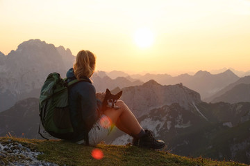 LENS FLARE: Unrecognizable girl observes the sunset above the Alps with her dog.