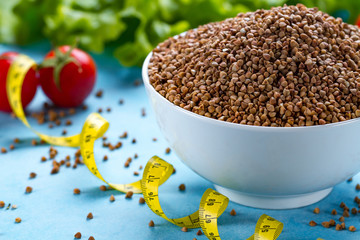 Buckwheat bowl with fresh ripe vegetables and yellow measuring tape. Buckwheat cereal grains for dietary, healthy eating. Fiber and slimming food. Diet concept