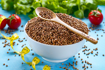 Buckwheat bowl and spoon with fresh ripe vegetables and yellow measuring tape. Buckwheat cereal grains for dietary, healthy eating. Fiber and slimming food. Diet concept