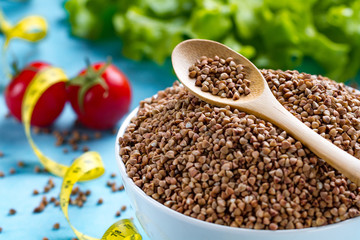 Buckwheat bowl and spoon with fresh ripe vegetables and yellow measuring tape. Buckwheat cereal grains for dietary, healthy eating. Fiber and slimming food. Diet concept