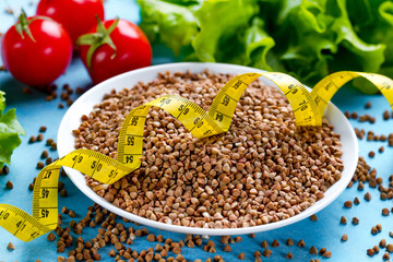 Buckwheat bowl with fresh ripe vegetables and yellow measuring tape. Buckwheat cereal grains for dietary, healthy eating. Fiber and slimming food. Diet concept