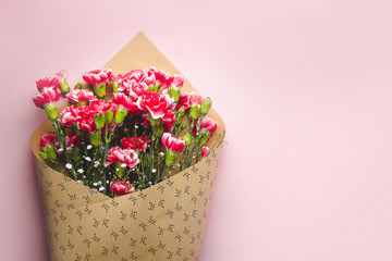 A bouquet of fresh carnations in craft paper on a pink background. Floristry. Congratulate and give flowers to woman on female holiday. Copy space