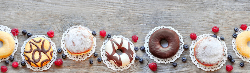 Dessert food top view banner.  Variety of donuts and berries on wooden background. .  Food concept, copy space.