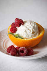 Closeup of a vanilla ice cream ball in an orange rug with raspberries on a white plate. Delicious sweet tropical dessert for the summer.