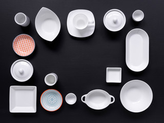 white and colorful tableware in different designs and sizes on black background, photographed from above in daylight