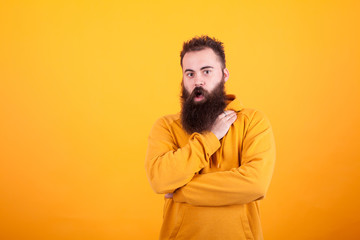 Portrait of beautiful bearded hipster looking amazed over yellow background