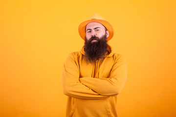 Bearded man with orange hat on his hat holding his arms crossed over yellow background