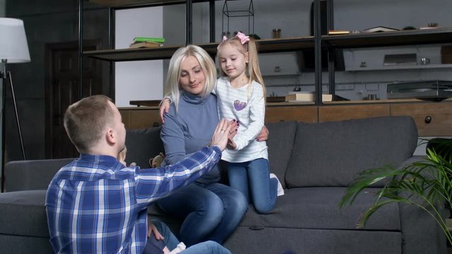 United family with cute daughters expressing connection and trust while touching hands at home. Toddler girl reaching to mom while older preschool sister touching dad's hand in domestic interior.