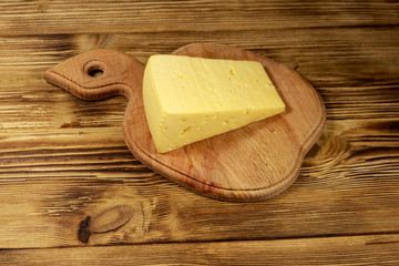 Piece of cheese on cutting board on wooden table