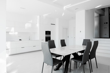 Fototapeta na wymiar Luxurious modern dining room with white table, black chairs and white modern kitchen. Minimalistic style.
