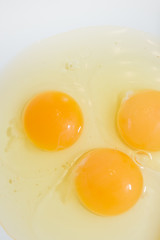 Three broken chicken eggs in a white mixing bowl