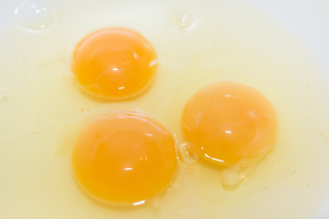 Three broken chicken eggs in a white mixing bowl