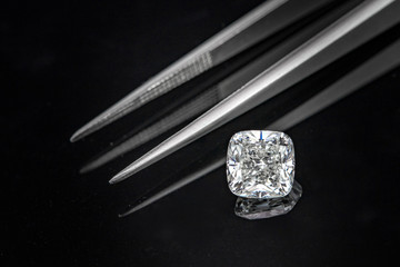 Cushion cut diamond with tweezers on black reflection background