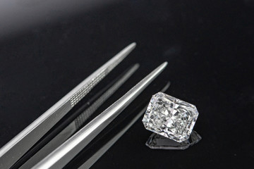 Radiant cut diamond with tweezers on black background