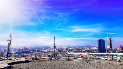 Obraz premium Mobile telecommunication cellular radio network antennas on a mast on the roof broadcasting signal waves over the city on a clear sunny day with blue sky and clouds