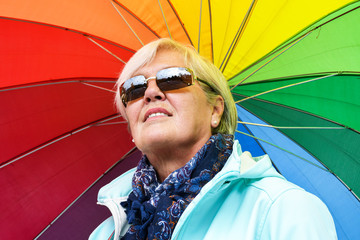 Middle aged grey haired woman holding colorful umbrella outside on a sunny day in autumn  - Powered by Adobe