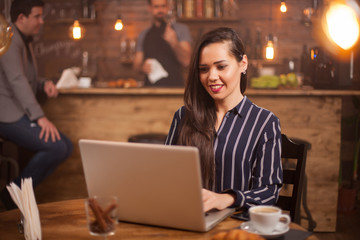 Smiling woman browsing on her laptop in a vintage coffee shop