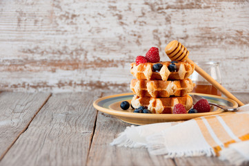 Traditional waffles with fresh  raspberries and blueberries on lace doily on wooden background. ...